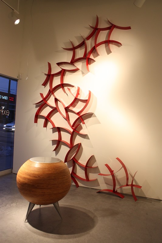 A red metal sculpture on wall, and a round wood coffee talbe